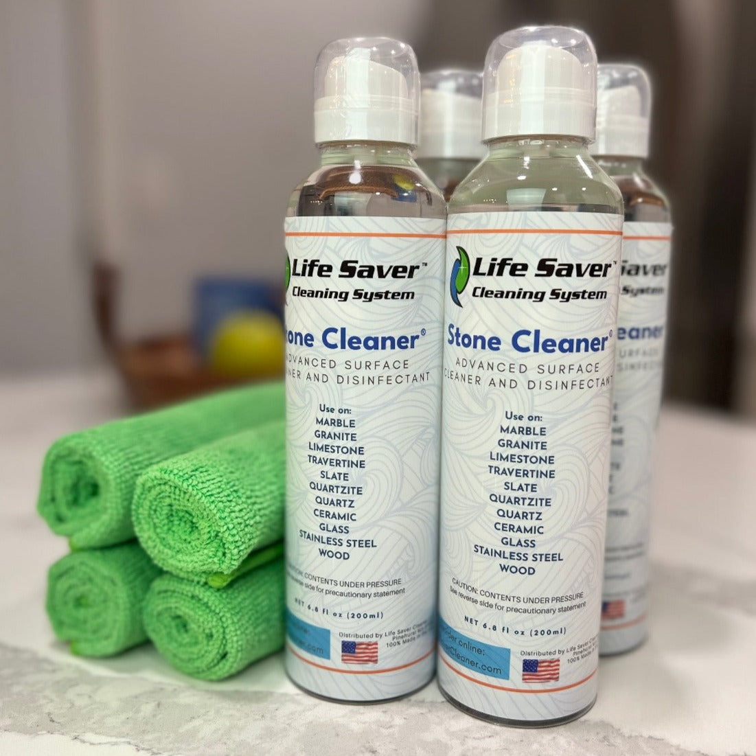 Four pack of Life Saver Stone Cleaner 6.8oz clear bottles with four Life Saver Mini Cloths on white Quartz countertop