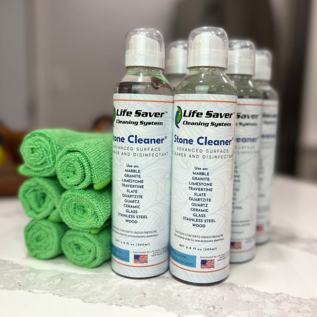 Six pack of Life Saver Stone Cleaner 6.8oz clear bottles with six Life Saver Mini Cloths on white Quartz countertop